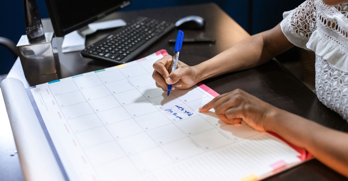 Une personne notant un rendez-vous sur un calendrier de bureau au stylo