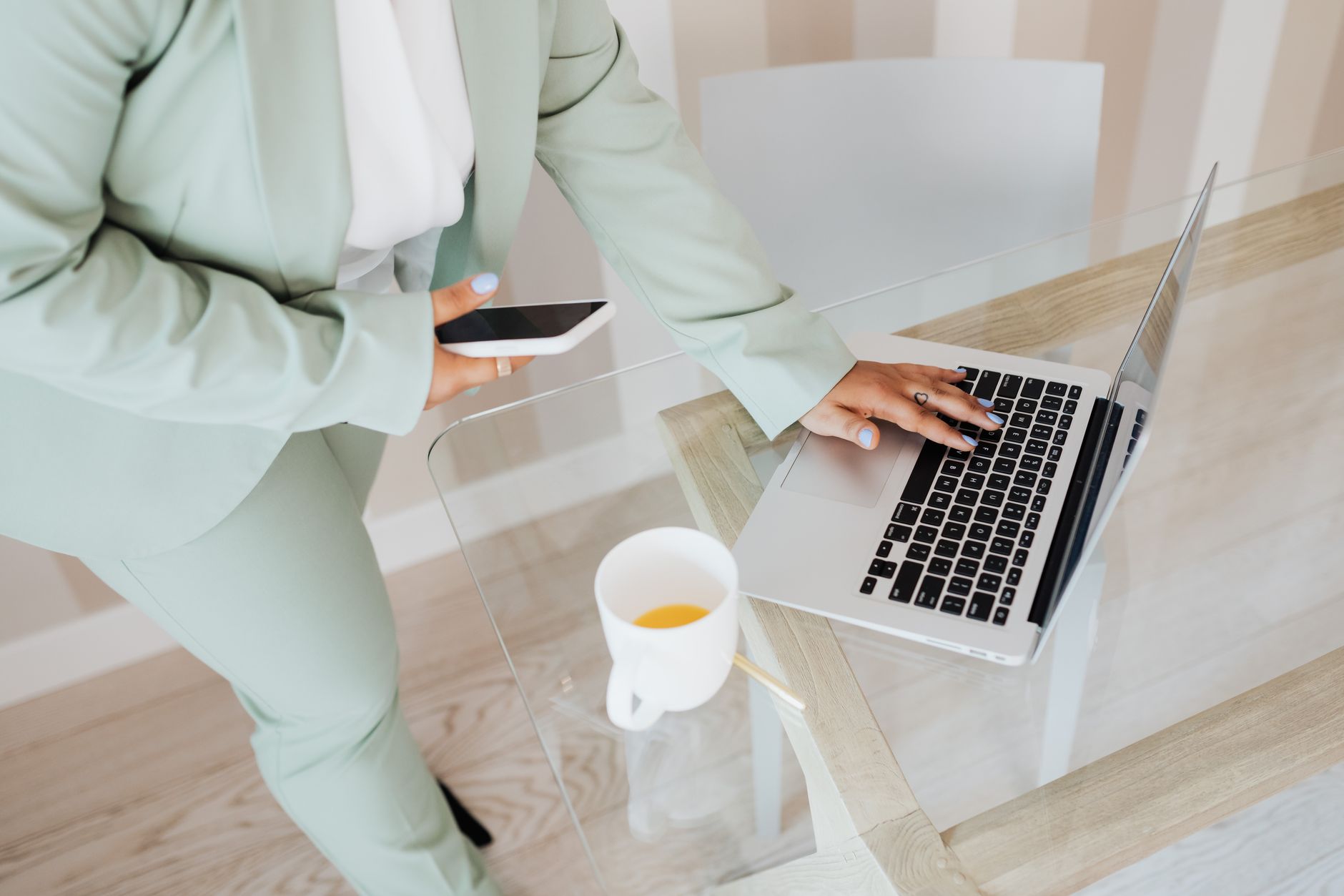 Une personne utilise un smartphone et un ordinateur portable sur un bureau en verre, illustrant les deux canaux emailing et SMS