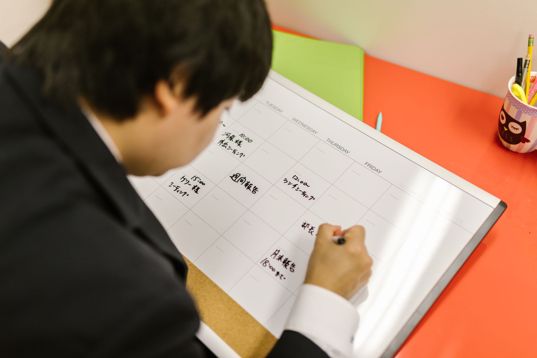Personne qui écrit dans un agenda hebdomadaire posé sur un bureau pour organiser son planning